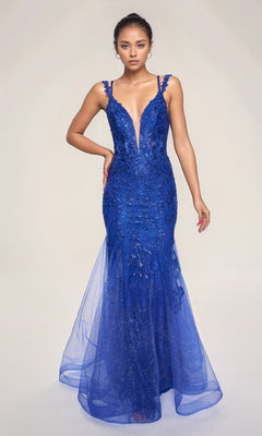 A woman stands against a plain background in the Nina Canacci 7600 Lace Mermaid Prom Dress, featuring a fitted deep blue design with a plunging neckline and subtle sparkling embellishments.