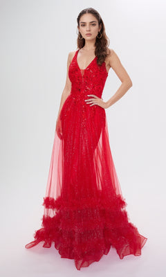 A woman wears the Nina Canacci 7607, a sleeveless floor-length red sequin formal dress with a deep V-neckline, fitted silhouette, and tulle ruffles at the hem, standing against a plain background.