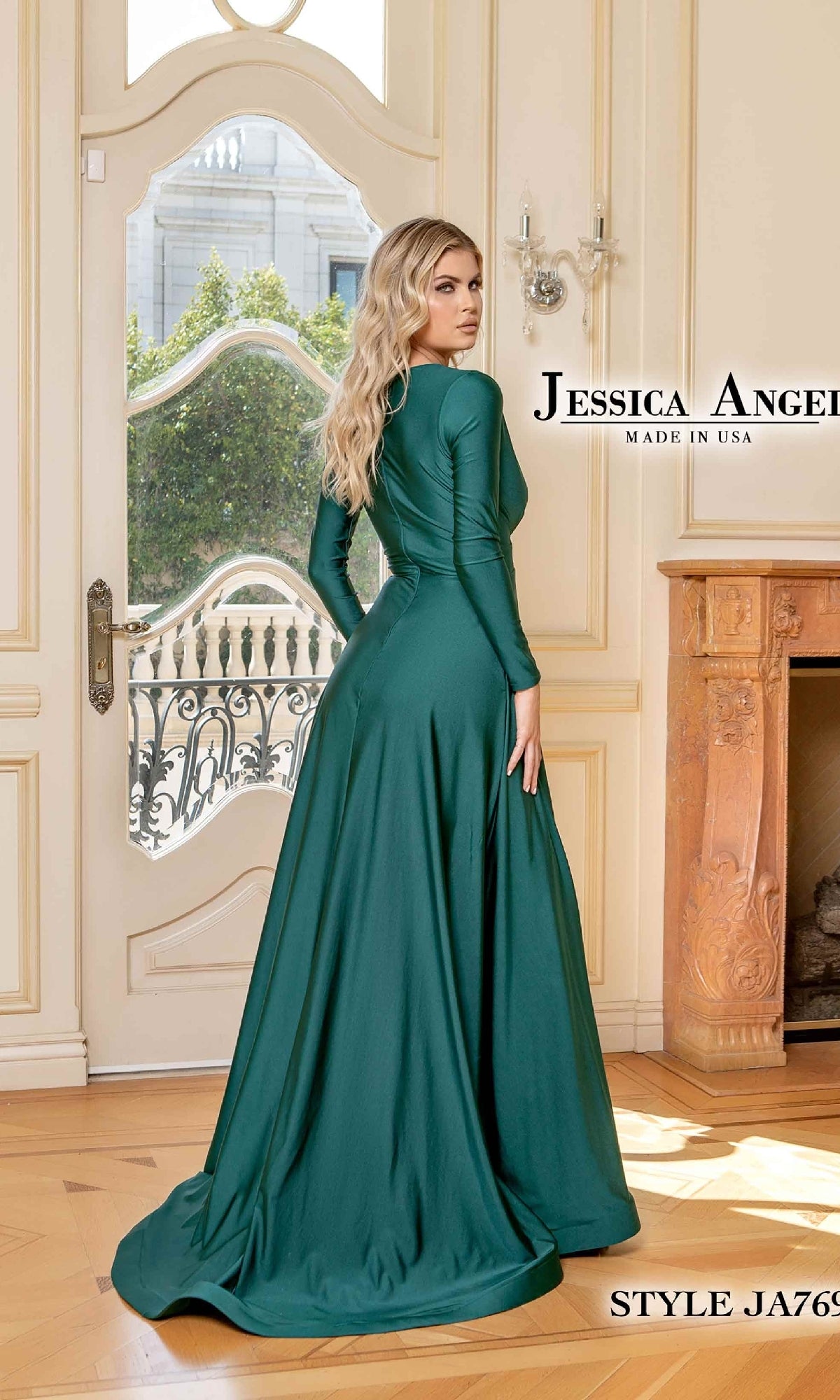 A woman faces away indoors, her head turned to the side, wearing a long-sleeve, floor-length emerald green formal dress—Jessica Angel 769. 