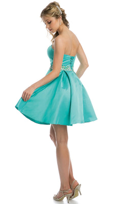 A woman stands in profile, holding the skirt of the Juliet 769 short hoco dress—a strapless turquoise gown with a sweetheart neckline, lace-up back, and beading at the waist.