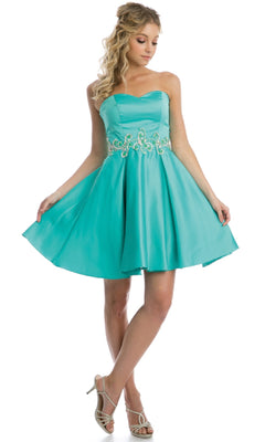 A woman poses in the Short Hoco Dress: Juliet 769, featuring a strapless sweetheart neckline, flared turquoise skirt, and beaded waist detail, paired with strappy high-heeled sandals.