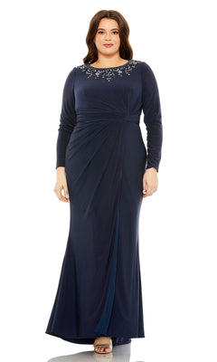 A woman stands facing forward in the Mac Duggal Long Plus-Size Prom Dress 77023—a navy blue, floor-length gown featuring long sleeves, a gathered waist, and an embellished neckline.