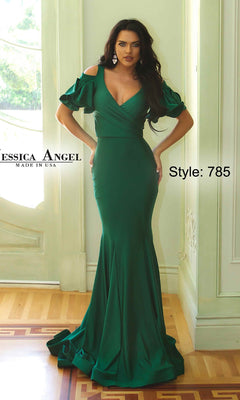 A woman in a Jessica Angel 785 Cold-Shoulder Long Prom Dress stands indoors near a window. The fitted, floor-length green gown features ruffled short sleeves and a graceful mermaid skirt. Text reads "Jessica Angel Made in USA" and "Style: 785.