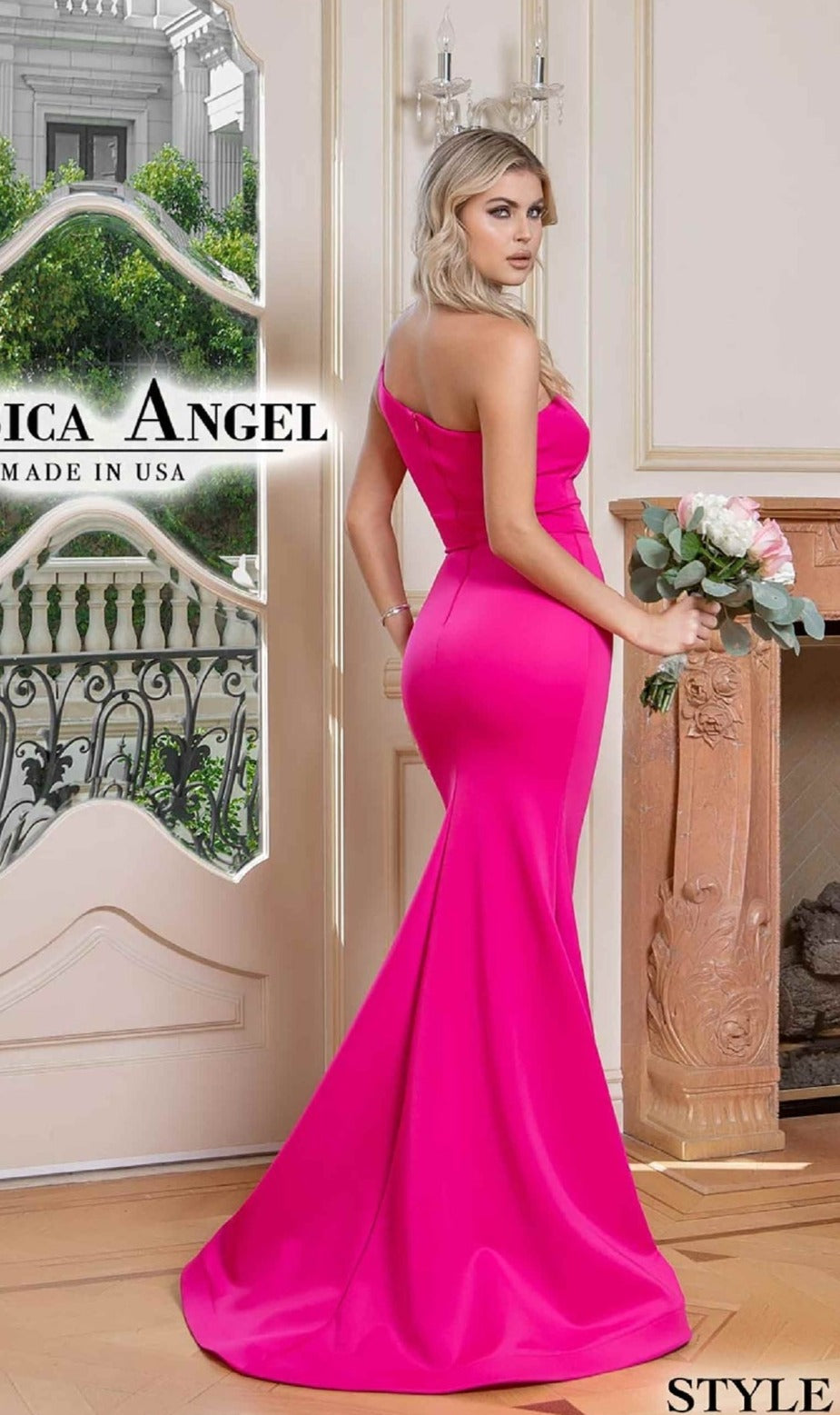 A woman stands indoors by a fireplace and large window, holding a bouquet and wearing the bright pink One-Shoulder Long Prom Dress: Jessica Angel 786, a stunning gown with a mermaid skirt that exudes elegance and modern charm.