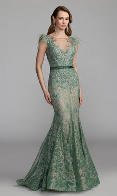A woman is wearing the Mac Duggal 79230 Feathered Long Lace Formal Dress in sage—a floor-length, sleeveless gown with floral embroidery and feathered shoulder accents—paired with drop earrings, standing against a plain gray background.