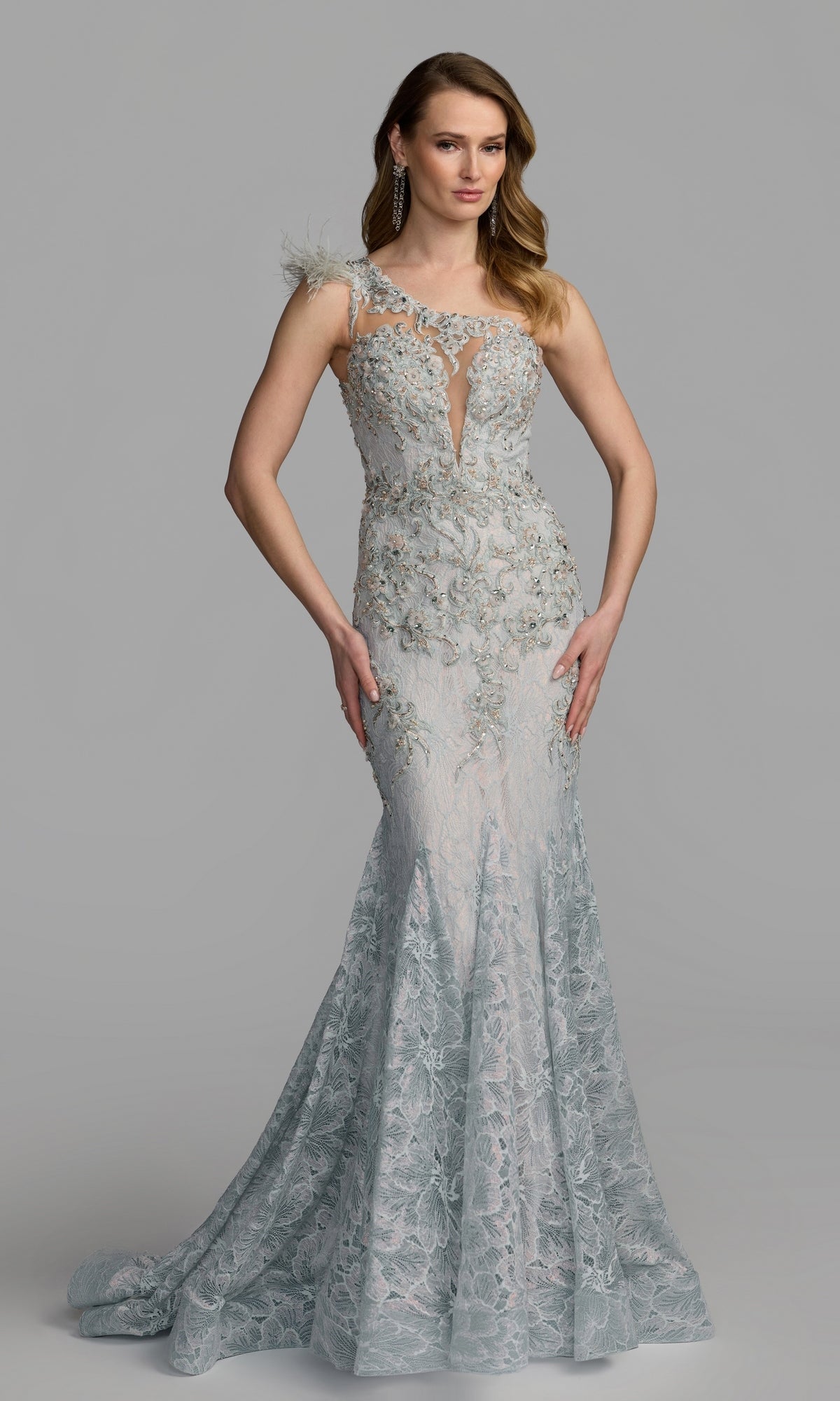A woman wearing the Mac Duggal 79264 Feather One-Shoulder Prom Gown in crystal blue, featuring elegant feather details and a striking one-shoulder design, stands against a plain gray background.