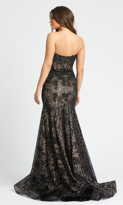 A woman models the Mac Duggal 79308 Strapless Black Lace Prom Gown, standing with her back to show off its fitted back and dramatic flared train.