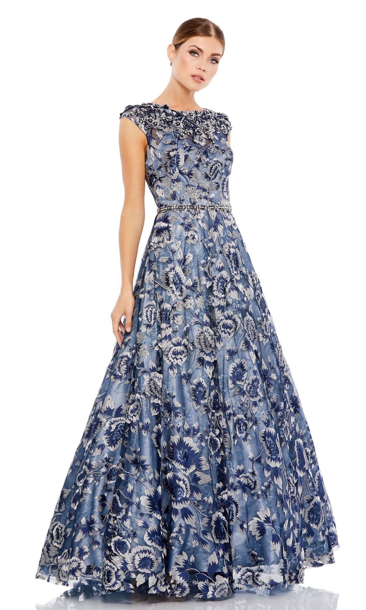 A woman models the Mac Duggal 79325 Cap-Sleeve Long Prom Ball Gown—blue with floral embroidery, cap sleeves, a fitted waist, and a floor-length skirt—standing against a plain white background.