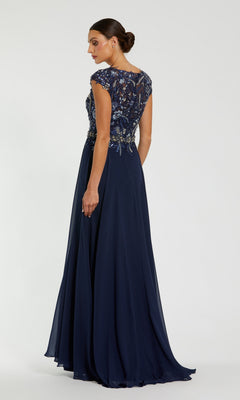 A woman wearing the Mac Duggal 79365 Cap-Sleeve Long Formal Dress in navy blue, featuring an embellished bodice, stands facing away and looks over her shoulder against a plain background.