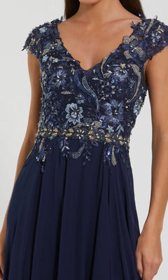 A woman in the Mac Duggal 79365 Cap-Sleeve Long Formal Dress in navy blue, with an embellished bodice featuring intricate floral embroidery and beaded cap sleeves.