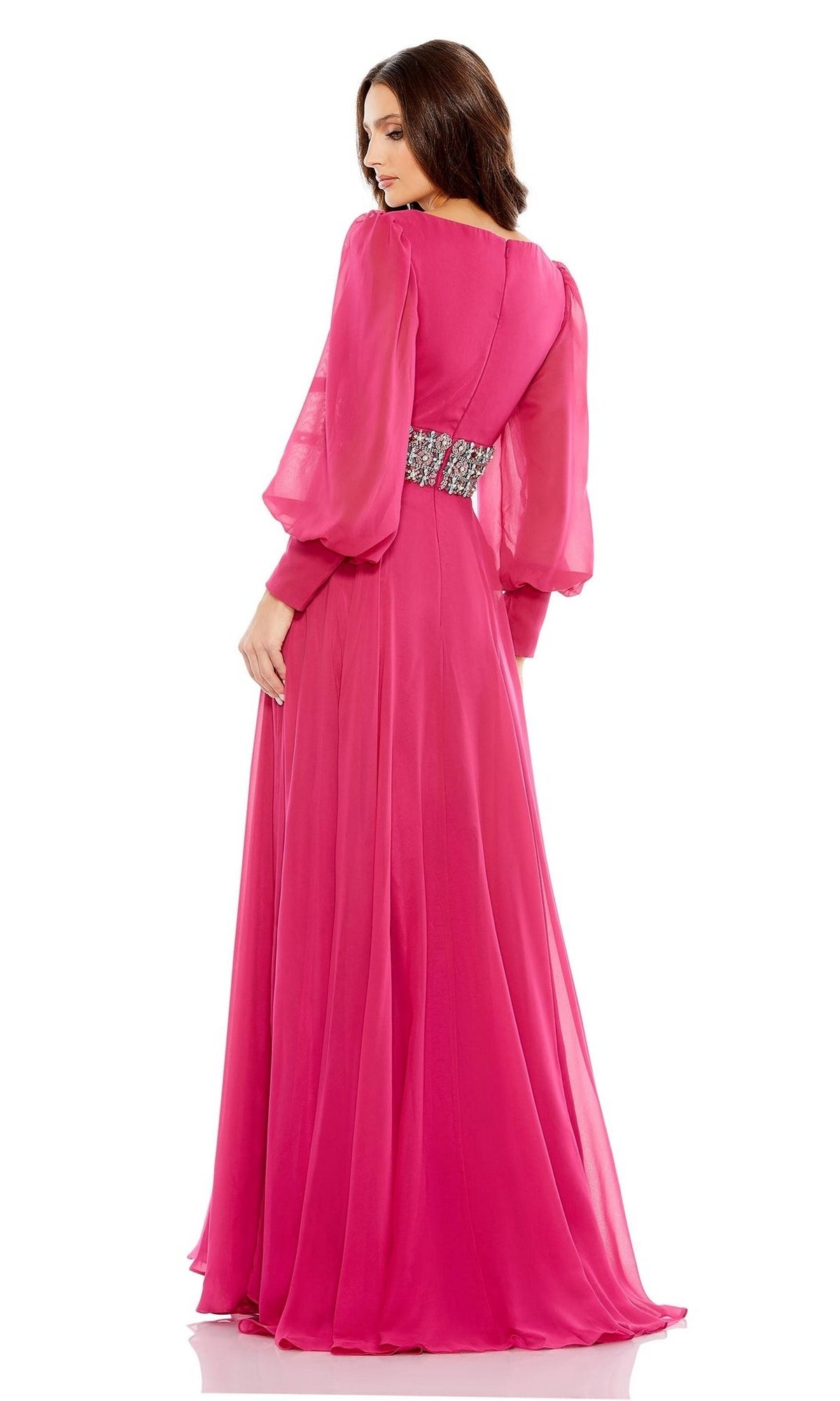 A woman stands looking over her shoulder in the Mac Duggal 79390—a long-sleeved, floor-length pink formal dress with sheer sleeves and an embellished waistband—an elegant pick for the mother of the bride.