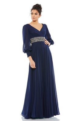 A woman models the Mac Duggal 79390 long sleeve formal evening dress in navy blue, featuring sheer sleeves and an embellished waistband, against a plain white background.