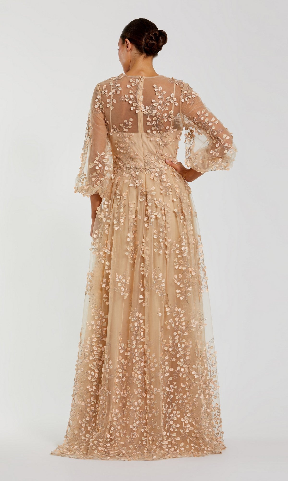 A woman stands facing away, her hair in a neat bun, wearing the Mac Duggal 79399 long sleeve blue formal dress with sheer nude fabric and floral embroidery.