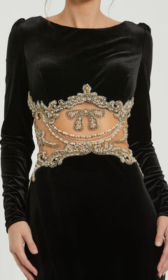 A woman wears the Mac Duggal 79445 long black formal dress, featuring a beaded sheer midriff adorned with intricate gold and pearl embroidery.