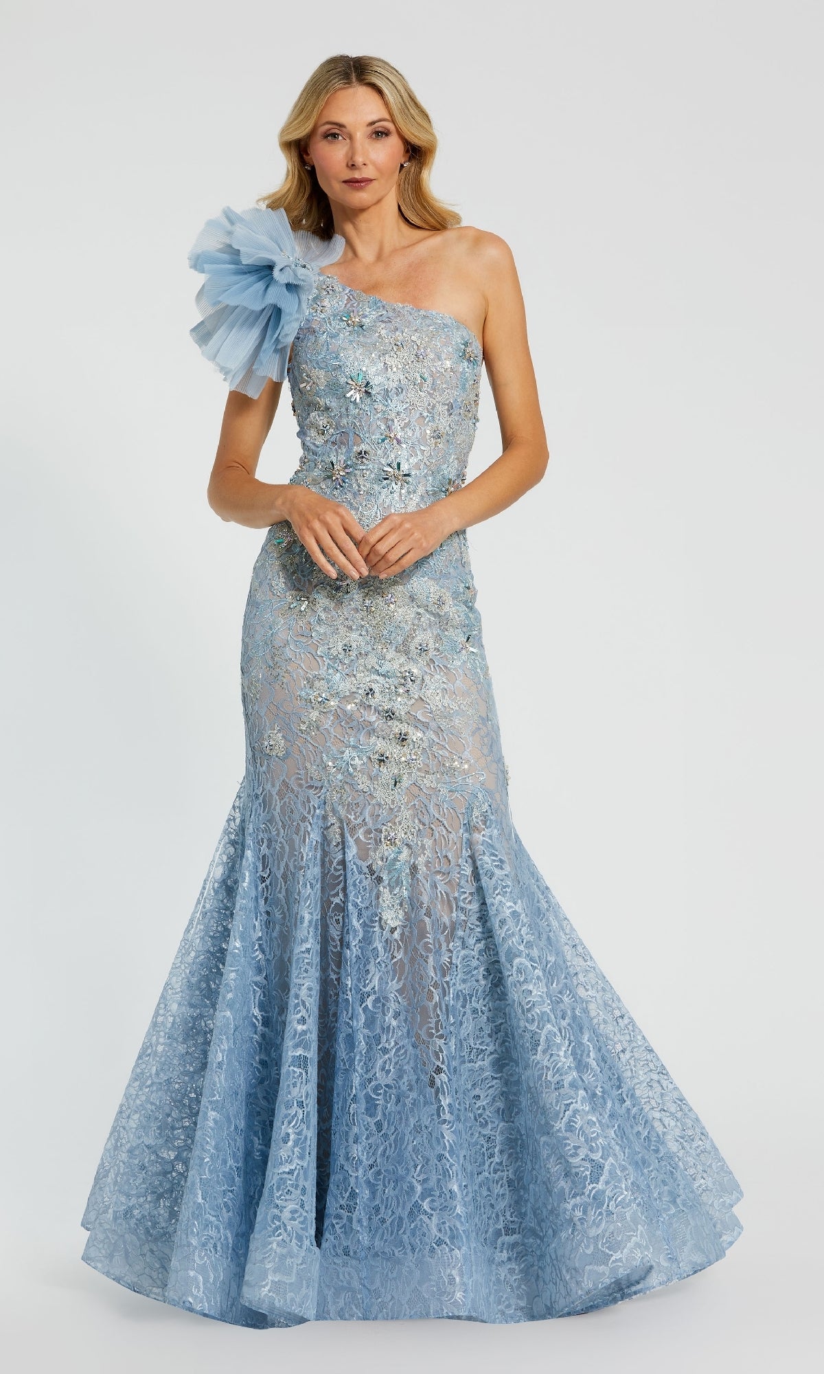 A woman stands against a plain background wearing the Mac Duggal 79456, a light blue one-shoulder long formal dress featuring lace details, a mermaid silhouette, and a dramatic tulle shoulder ruffle.