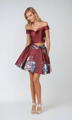 A woman in the Juliet 798 short party dress—burgundy off-shoulder top with a matching floral A-line skirt—stands against a light background, accessorized with a pearl necklace and white heels.