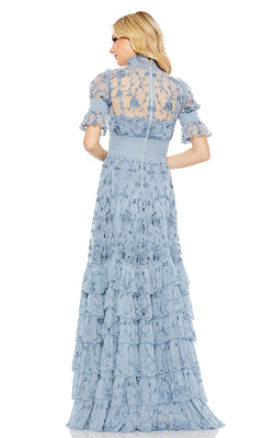 A woman with blonde hair models the Mac Duggal 8005—a floor-length, light blue lace evening gown with short sleeves, floral embroidery, and tiered ruffles—shown from the back.