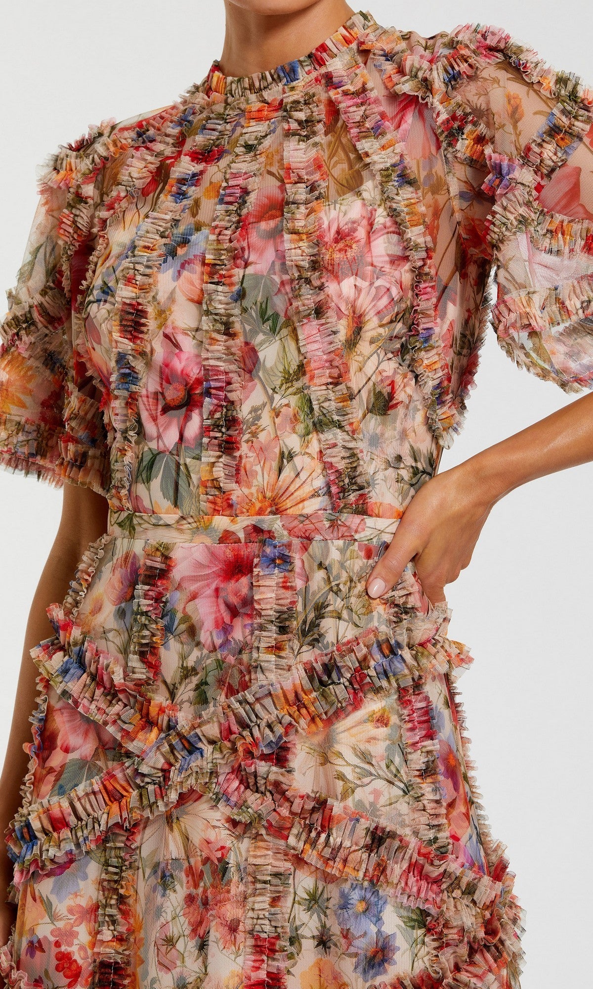 A person wears the Mac Duggal 8010 Short-Sleeve Wedding-Guest Dress, featuring sheer fabric, multicolored ruffle trim, and delicate floral-print patterns; only the upper body and part of the arm are shown.