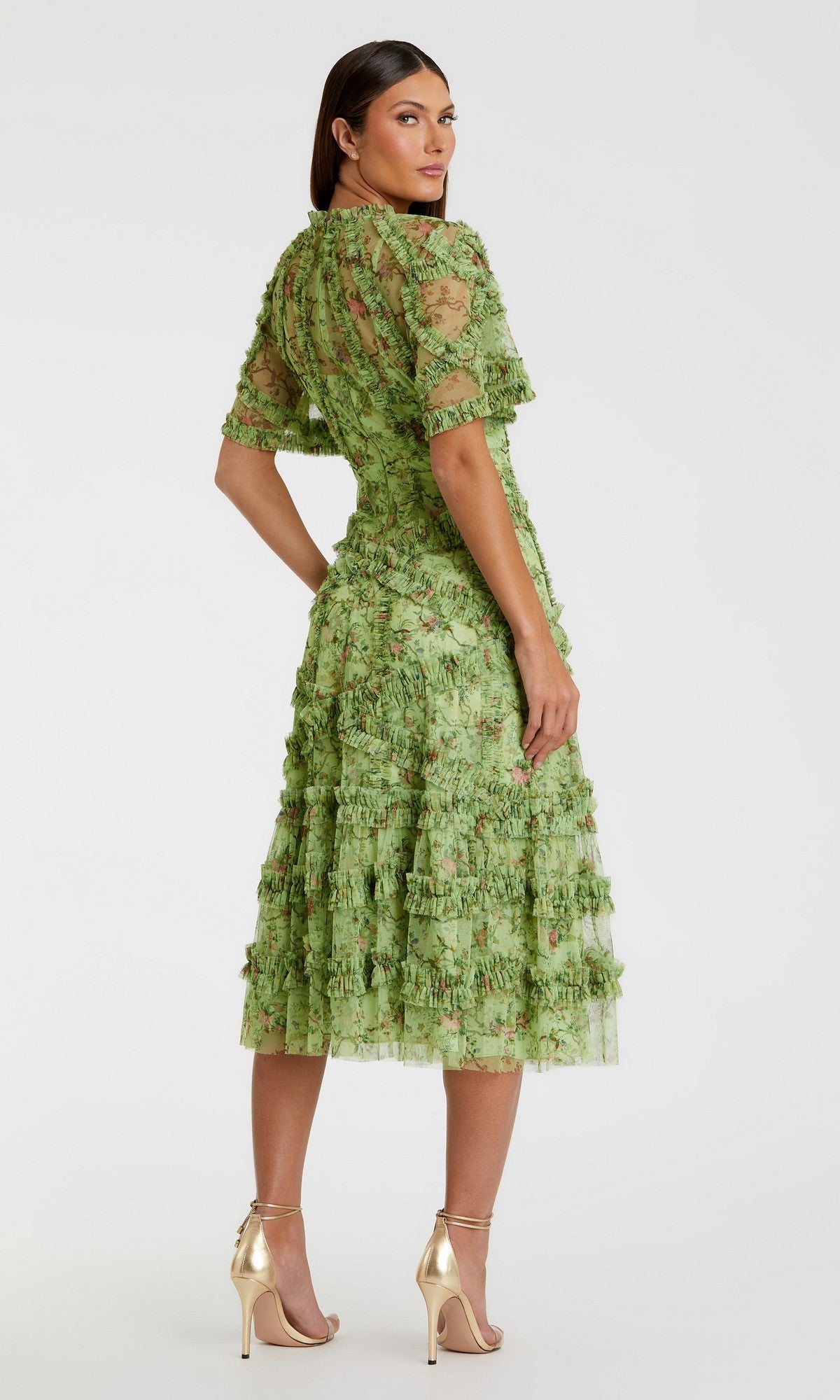 Woman wearing the Mac Duggal 8010 short-sleeve wedding-guest dress, green and textured, paired with gold high-heeled sandals, standing and looking over her shoulder.