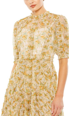 A woman is shown from the waist up wearing the Mac Duggal 80111 short sleeve wedding guest dress, a high-neck midi style featuring a floral print with yellow and green ruffle accents.