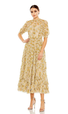 A woman wears the Mac Duggal 80111 Short Sleeve Wedding Guest Dress, a light yellow floral midi with puff sleeves, paired with metallic high-heeled sandals, standing against a plain white background.