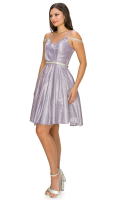 A woman in the Beaded Cold-Shoulder Short Homecoming Dress 8014J, a lavender knee-length dress with shimmer and beaded accents, paired with silver high-heeled sandals, stands against a white background.
