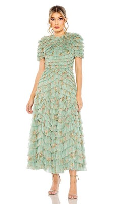 A woman showcases the Midi Wedding Guest Dress 8014 by Mac Duggal—sage green with ruffled tulle layers and floral embellishments—paired with strappy heels for an elegant semi-formal look against a white background.