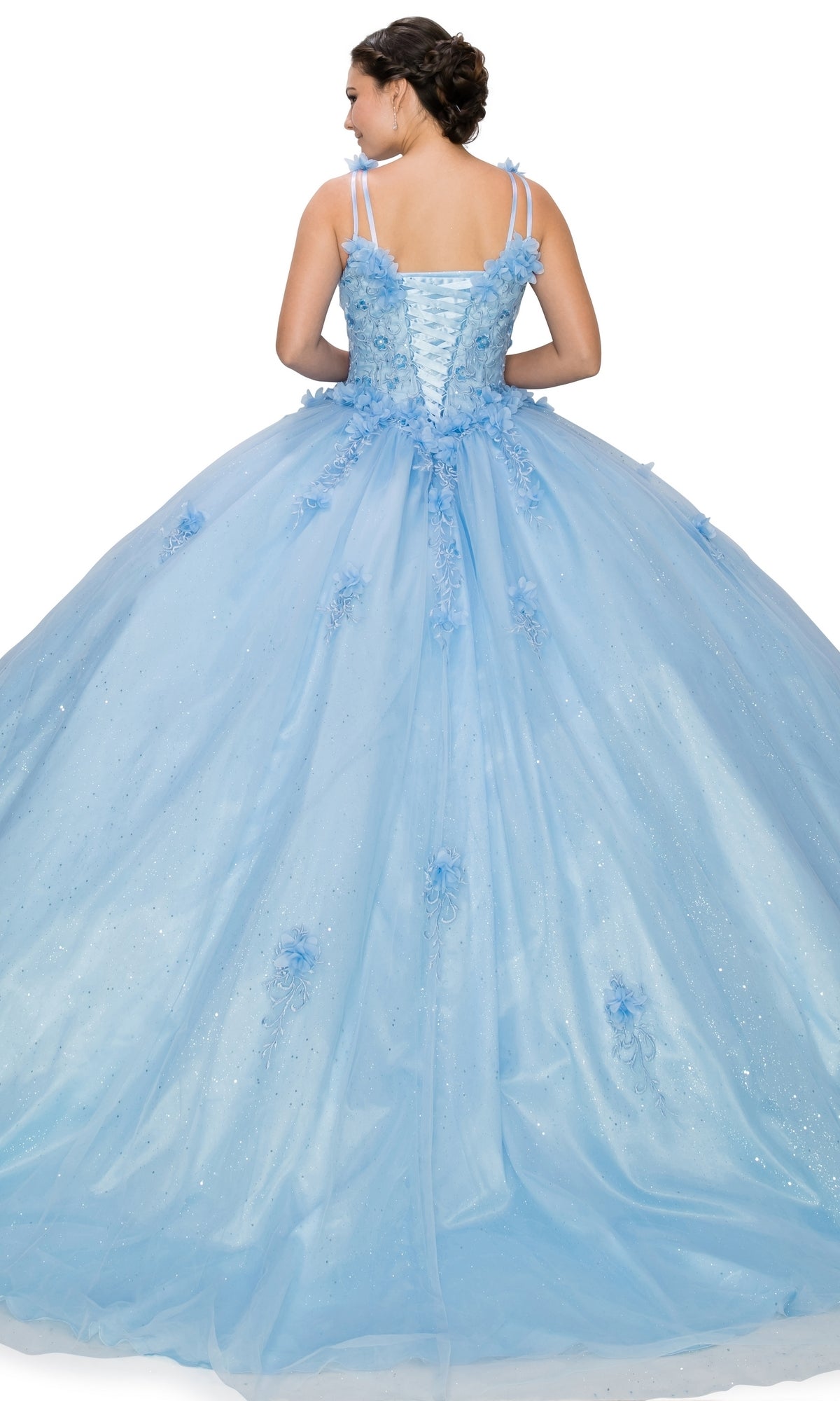 A woman wearing the Quinceanera Ball Gown 8025J, featuring light blue fabric, floral embellishments, embroidered lace details, and a lace-up back, stands with her back to the camera.