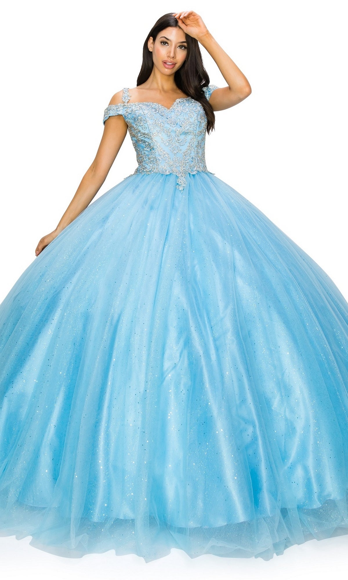 A woman wears the Quinceanera Ball Gown 8028J, a light blue off-the-shoulder dress with a glitter tulle ball gown skirt and lace bodice, standing against a white background.