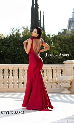 A woman in a sleeveless, backless red Backless Long V-Neck Prom Dress: Jessica Angel 803 stands on a stone patio with greenery and trees behind her. "Made in USA" is displayed in the text.