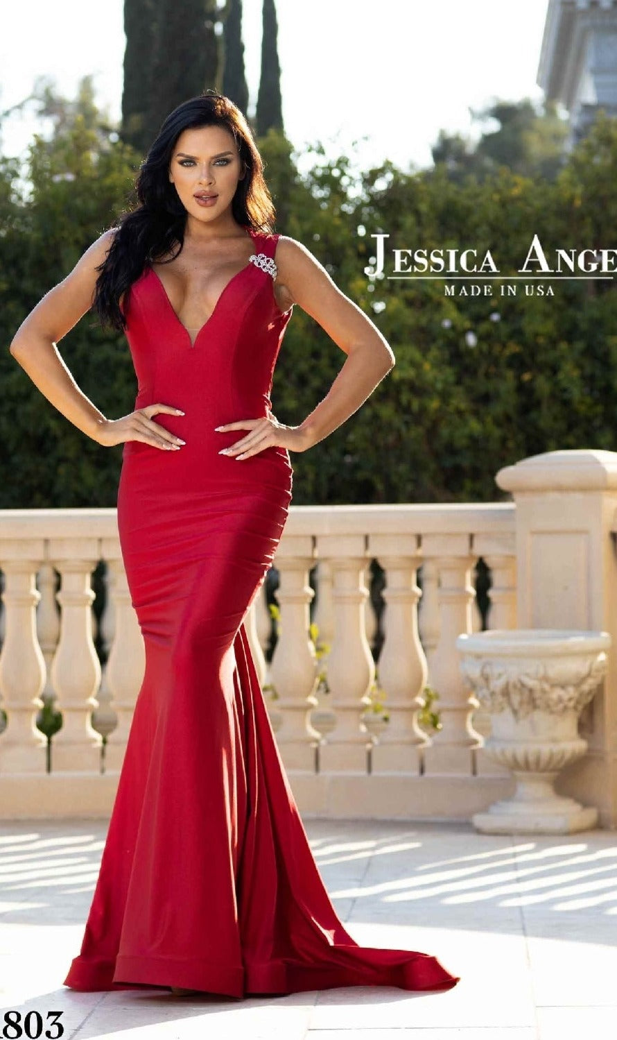 Woman in a fitted, sleeveless red Backless Long V-Neck Prom Dress: Jessica Angel 803, standing outdoors by a stone balustrade. Made in USA.