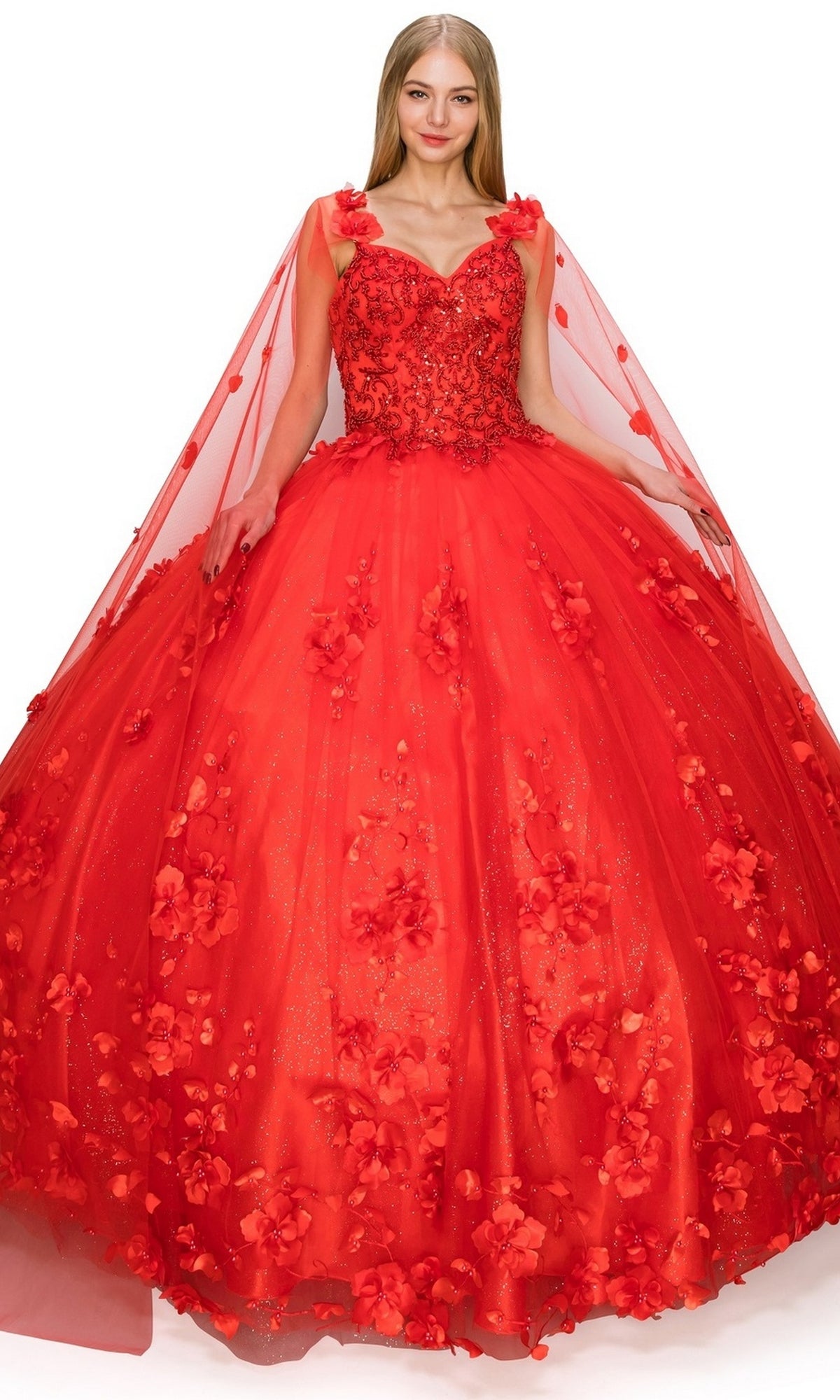 A woman wears the Quinceanera Ball Gown 8030J, featuring a bright red hue, 3D floral embellishments, a fitted bodice, and a sheer cape, standing against a white background.