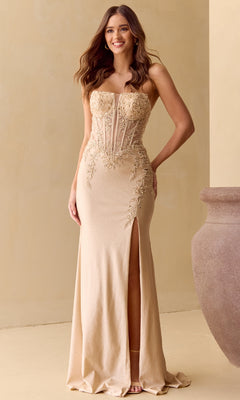 A woman wearing the Long Glitter Prom Dress: Amelia Couture 8040, a strapless gold gown with floral embroidery, high slit, and sheer bodice detailing, stands indoors beside a large decorative vase.
