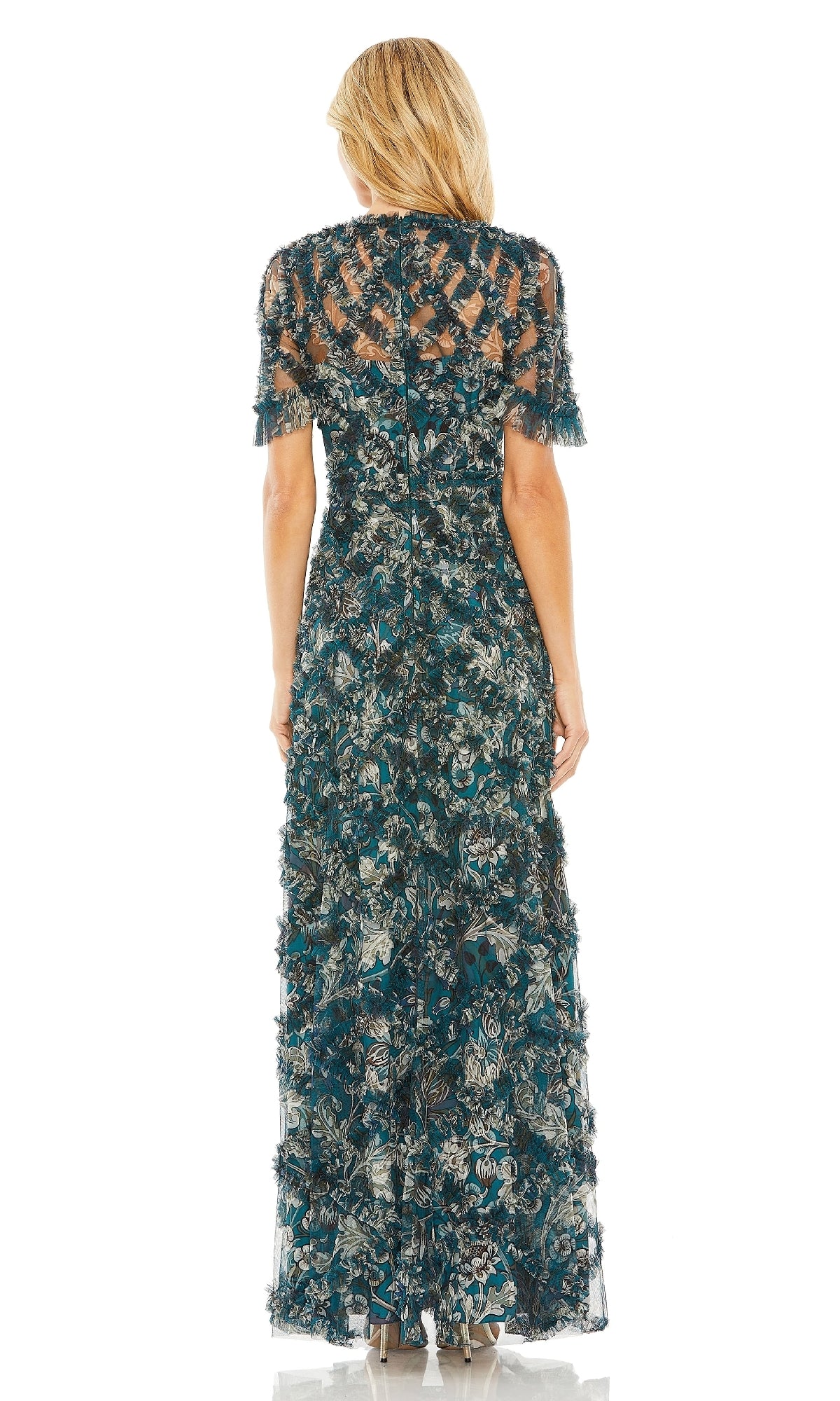 A woman stands facing away, wearing the Mac Duggal 8043 long formal dress, featuring short sleeves and a detailed blue, green, and beige floral pattern.