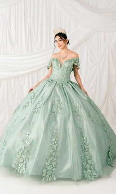 A woman wearing the Quinceanera Ball Gown 8045J with glitter lace embroidery, 3D floral details, a tiara, and a necklace stands in front of draped white fabric.