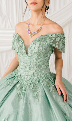 A woman wearing the Quinceanera Ball Gown 8045J with glitter lace embroidery and 3D floral detail, plus a beaded necklace and earrings, stands before a white draped backdrop.