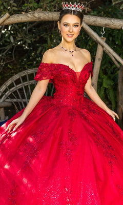 A woman wearing the Quinceanera Ball Gown 8045J with sparkling red glitter lace embroidery and a tiara stands outdoors before a wooden arch and greenery.