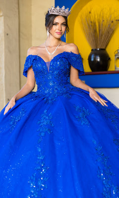 A woman in the Quinceanera Ball Gown 8045J with glitter lace embroidery and a tiara stands indoors before a yellow and blue alcove.