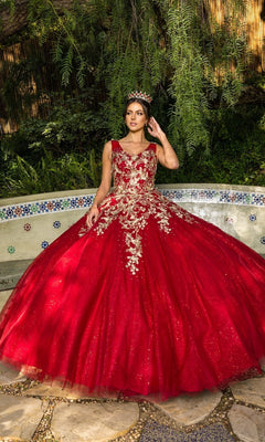 A young woman wearing the Quinceanera Ball Gown 8046J with metallic embroidery and a tiara stands outdoors by a decorative tiled bench amid lush greenery.