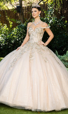 A woman stands outdoors wearing the Quinceanera Ball Gown 8046J, a light gold off-shoulder dress with metallic embroidery, floral embellishments, paired with a necklace and tiara.