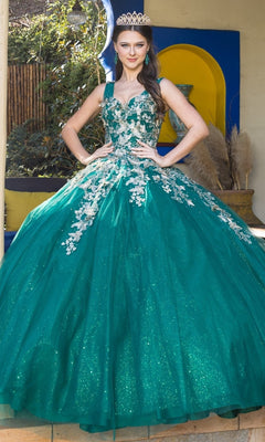 A young woman in the Quinceanera Ball Gown 8046J, featuring glitter tulle and 3D butterfly details with a tiara, stands outdoors posing confidently with her hands on her waist in front of colorful decor.