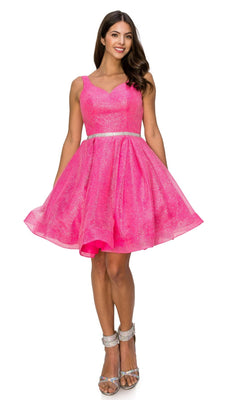 A woman stands smiling in the Short Glitter Princess Homecoming Dress 8047J—sleeveless, knee-length, bright pink with sparkling texture—paired with a silver belt and silver high-heeled sandals.