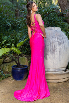 A woman wearing the Strappy-Back Embellished Long Prom Dress 8048J, a bright pink gown with beaded straps and lace-up back, stands outdoors near a large decorative vase and lush green plants.