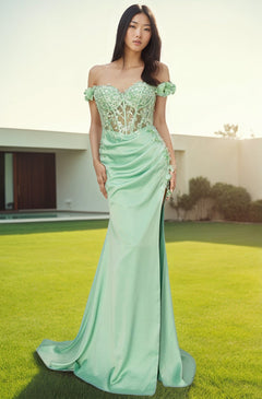 A woman stands on a lawn wearing the Off-the-Shoulder Floral Embroidered Prom Dress 8050J in light green, featuring a sheer lace bodice and long fitted skirt, with a modern building visible in the background.