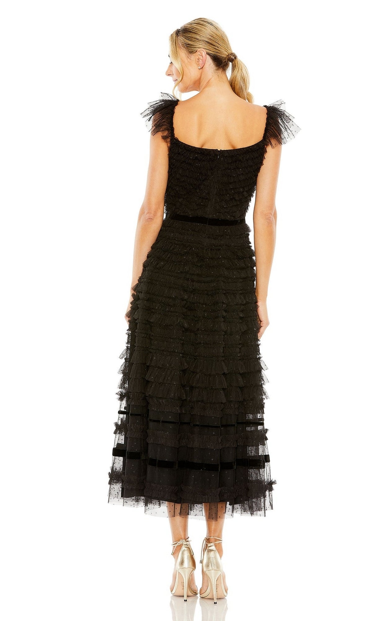 A woman faces away from the camera in a black Mac Duggal 8054 midi wedding guest dress with ruffles and silver heels, set against a white background.