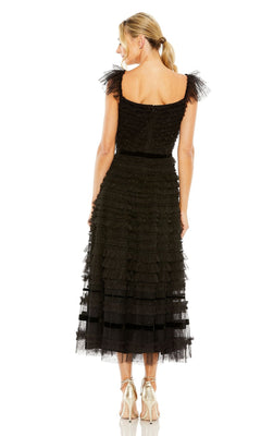 A woman faces away from the camera in a black Mac Duggal 8054 midi wedding guest dress with ruffles and silver heels, set against a white background.