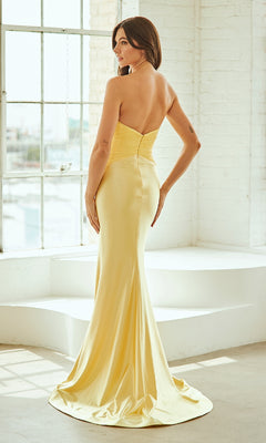 Woman modeling the back of a yellow evening gown standing in front of a large window in a white room.