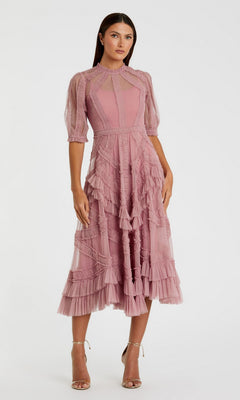 A woman in the Mac Duggal 8058 Ruffled Midi Wedding-Guest Dress in Antique Rose, featuring ruffled and sheer accents, stands in strappy high-heeled sandals against a plain light background.