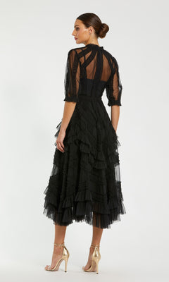 A woman stands facing away from the camera against a plain white background, wearing the Mac Duggal 8058 Ruffled Midi Wedding-Guest Dress with sheer sleeves and ruffled details, paired with gold high-heeled sandals.