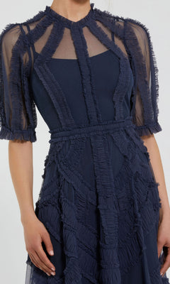 A woman wears the Mac Duggal 8058 Ruffled Midi Wedding-Guest Dress in navy blue, featuring sheer mesh panels, ruffled texture, short sleeves, and a fitted waist.